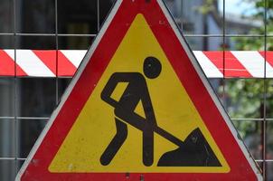 Das im Bau befindliche Warnschild ist mit einem rot-weiß gestreiften Signalband an einem Metallgitterzaun befestigt foto