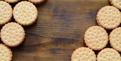 Ein runder Sandwichkeks mit Kokosfüllung liegt in großen Mengen auf einer braunen Holzoberfläche. Foto von essbaren Leckereien auf einem hölzernen Hintergrund mit Kopierraum