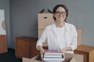 lächelnde hispanische weibliche Büroangestellte, die Dinge am Umzugstag verpackt. neue Wohnung, Umzugskonzept foto