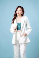 Halbkörper einer selbstbewussten, eleganten, schönen asiatischen Geschäftsfrau, die einen weißen Anzug trägt und auf isoliertem blauem Hintergrund posiert. junge shopaholic-frau auf kopienraum. foto