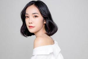 kurze haare der asiatischen frau mit perfekter sauberer frischer haut. süßes weibliches Modell mit natürlichem Make-up und funkelnden Augen auf weißem, isoliertem Hintergrund. gesichtsbehandlung, kosmetik, schönheitskonzept. foto