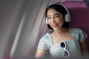 porträt einer erfolgreichen asiatischen geschäftsfrau in einem flugzeug sitzt in einem business-class-sitz und verwendet einen um-ohr-kopfhörer zum abspielen von musik während des fluges. Relax-Konzept foto