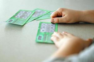 Nahaufnahme der Silbermünze in der Hand des Spielers, der eine gefälschte Lotteriekarte kratzt. lotteriespielkonzept, kratzkartenlotterie foto