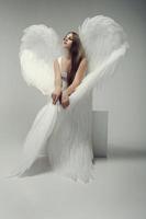 ein romantisches engelsmädchen mit weißen flügeln posiert sitzend