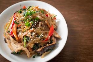 Japchae oder gebratene koreanische Fadennudeln mit Gemüse und Schweinefleisch, garniert mit weißem Sesam foto