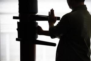 Silhouette eines Fighter Wing Chun und einer Holzpuppe auf einem Hintergrund. Wing Chun Kung Fu Selbstverteidigung foto