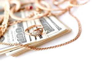 Viele teure goldene Schmuckringe, Ohrringe und Halsketten mit einer großen Menge US-Dollar-Scheine auf weißem Hintergrund. Pfandhaus oder Juweliergeschäft foto