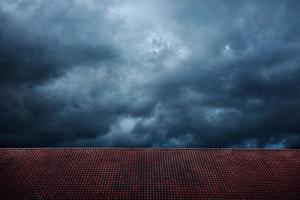 dunkler dramatischer himmel vor regen und sturm. Zyklon kommt mit schwarzer windiger Wolke. Hausabdeckung durch rotes Ziegeldach als Vordergrund. Wetter- und Jahreszeitenwechsel foto