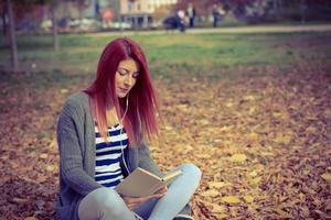 schöne rothaarige frau, die sich mit buch und musik im park entspannt. foto