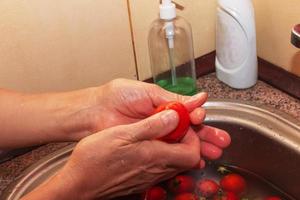 Die Hände der Frau waschen die Tomaten und entfernen die Stiele vom Gemüse. foto