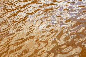 Illustration des Wasserkräuselungsbeschaffenheitshintergrundes. Wellenförmige Wasseroberfläche bei Sonnenuntergang, goldenes Licht, das sich im Wasser spiegelt. foto