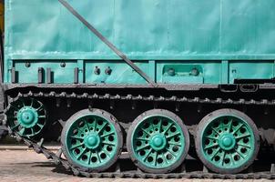 Seitenansicht des Fahrzeugs auf einer Raupenkette mit schwarzen Ketten und grünen Rädern und einer seitlichen Metallwand foto