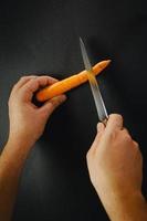 zwei Hände und Messer schneiden eine Karotte