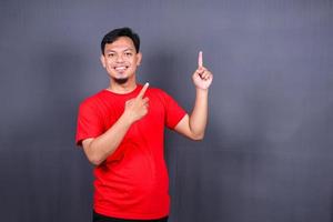 asiatischer junger mann im roten t-shirt, das mit seinem finger lokalisiert auf grauem hintergrund zeigt foto