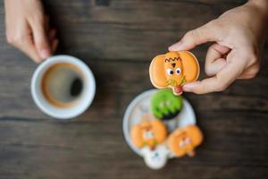 Hand, die eine Kaffeetasse hält, während sie lustige Halloween-Kekse isst. glücklicher halloween-tag, trick oder bedrohung, hallo oktober, herbstherbst, traditionelles, party- und feiertagskonzept foto