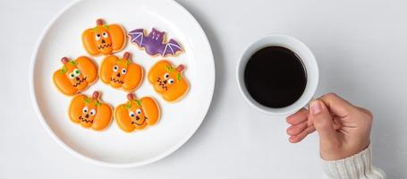 Frauenhand, die Kaffeetasse hält, während sie lustige Halloween-Plätzchen isst. Happy Halloween Day, Trick or Threat, Hallo Oktober, Herbstherbst, Traditions-, Party- und Urlaubskonzept foto