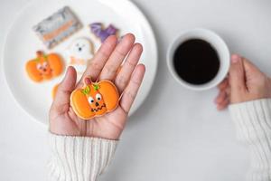 Frauenhand, die lustiges Halloween-Plätzchen beim Kaffeetrinken hält. Happy Halloween Day, Trick or Threat, Hallo Oktober, Herbstherbst, Traditions-, Party- und Urlaubskonzept foto