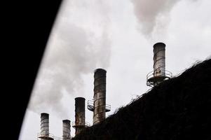 industrielle schornsteine, die hinter einem zaun rauch verschmutzen foto