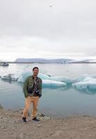 Mann steht vor der Jökulsarlon-Gletscherlagune in Island mit Eisbergen und klarem Wasser foto