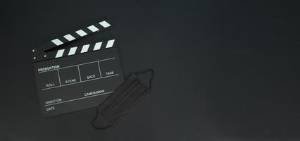 Filmklappe oder Filmtafel mit schwarzer Gesichtsmaske oder medizinischer Maske isoliert. es wird in der film-, filmproduktions- und kinoindustrie auf schwarzem hintergrund verwendet. covid-19 oder soziales distanzkonzept. foto