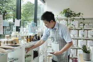 Asiatischer männlicher Ladenbesitzer überprüft den Bestand an natürlichen Bio-Produkten in der Schaufensterauslage im Nachfüllladen, abfallfreies und plastikfreies Lebensmittel, umweltfreundliche, nachhaltige Lebensstile, wiederverwendbarer Laden. foto