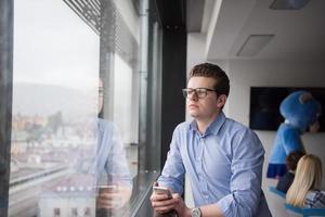 geschäftsmann, der in einem modernen gebäude nahe dem fenster mit telefon steht foto