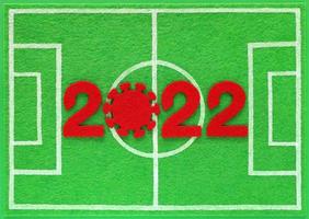 Roter Filz Neujahrszahlen 2022, Null in Form eines Corona-Virus, platziert auf Mini-Fußballfeld aus grünem Filz, Draufsicht. konzept über fußballmeisterschaft während einer covid-pandemie. foto