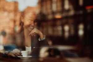 Frau in einem Café trinkt Kaffee, der durch Glas mit Reflexionen betrachtet wird, während sie an einem Tisch sitzen und plaudern und lachen foto