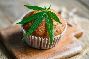 Cannabis-Lebensmittelkuchen mit Cannabisblatt-Marihuana-Kraut auf Holzhintergrund, köstliche süße Dessert-Cupcakes mit Hanfblattpflanze thc cbd-Kräuter-Food-Snack und medizinisches Konzept foto