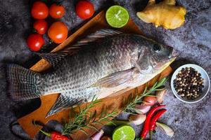 Tilapia mit Gewürz Rosmarin Tomate Zitrone Limette Ingwer Knoblauch Pfeffer Chili auf dunklem Hintergrund, frischer roher Tilapia-Fisch aus der Tilapia-Farm foto