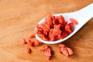 goji-beere trockene gewürze und kräuter dood zutaten - goji-beeren auf weißem löffel und holzhintergrund foto