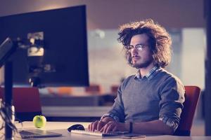 Mann, der im dunklen Büro am Computer arbeitet foto