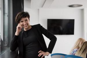 elegante Frau mit Handy durch Fenster im Bürogebäude foto