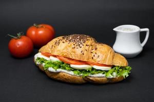 Vegetarisches Croissant mit Tomatenkäse und Salat auf schwarzem Hintergrund foto