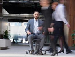 Geschäftsmann sitzt im Bürostuhl, Personengruppe vorbei foto