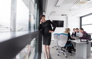 elegante Frau mit Handy durch Fenster im Bürogebäude foto