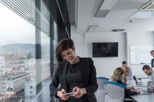 elegante Frau mit Handy durch Fenster im Bürogebäude foto