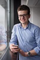 geschäftsmann, der in einem modernen gebäude nahe dem fenster mit telefon steht foto