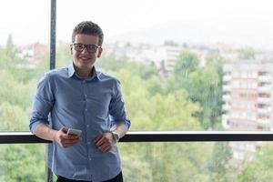 geschäftsmann, der in einem modernen gebäude nahe dem fenster mit telefon steht foto