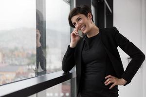 elegante Frau mit Handy durch Fenster im Bürogebäude foto