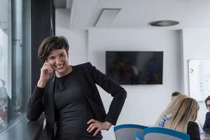 elegante Frau mit Handy durch Fenster im Bürogebäude foto