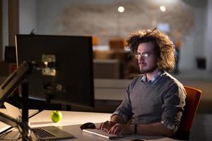 Mann, der im dunklen Büro am Computer arbeitet foto