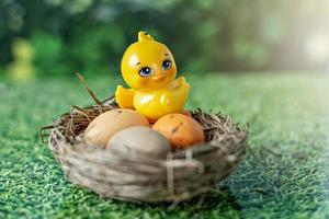 Ostereier in einem natürlichen Nest und dekoratives Huhn auf einem verschwommenen grünen Hintergrund mit Grasstruktur foto