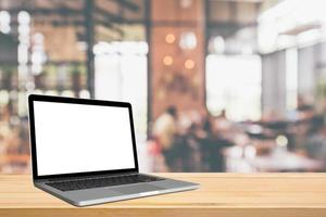 leerer weißer bildschirm laptop-computer auf holztischplatte mit café-restaurant abstraktem bokeh-licht defokussiertem unschärfehintergrund foto