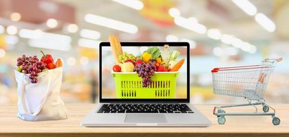 Supermarktgang verschwommenen Hintergrund mit Laptop-Computer und Einkaufswagen auf Holztisch Lebensmittelgeschäft Online-Konzept foto