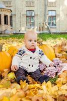 Kind im Strickpullover sitzt zwischen Kürbissen im Herbstpark foto