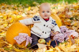 Kind im Strickpullover sitzt zwischen Kürbissen im Herbstpark foto
