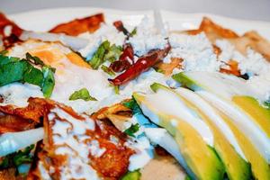 chilaquiles mexikanisches Essen mit roter Soße, Käse, Sahne und Chilischoten auf Vintage-Hintergrund foto
