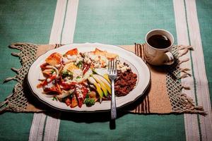 chilaquiles mexikanisches essen mit in roter soße, käse, sahne, chilischoten auf vintage hintergrund und kaffee foto