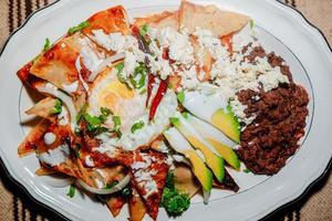 chilaquiles mexikanisches Essen mit roter Soße, Käse, Sahne und Chilischoten auf Vintage-Hintergrund foto